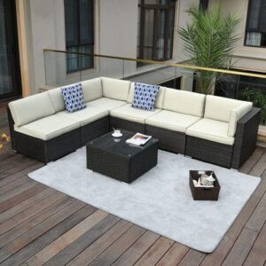 An outdoor wicker sofa with white cushions, situated on a wooden deck with a lush garden in the background."